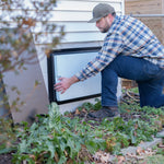 Man replacing insulation in crawl space door in a garden setting