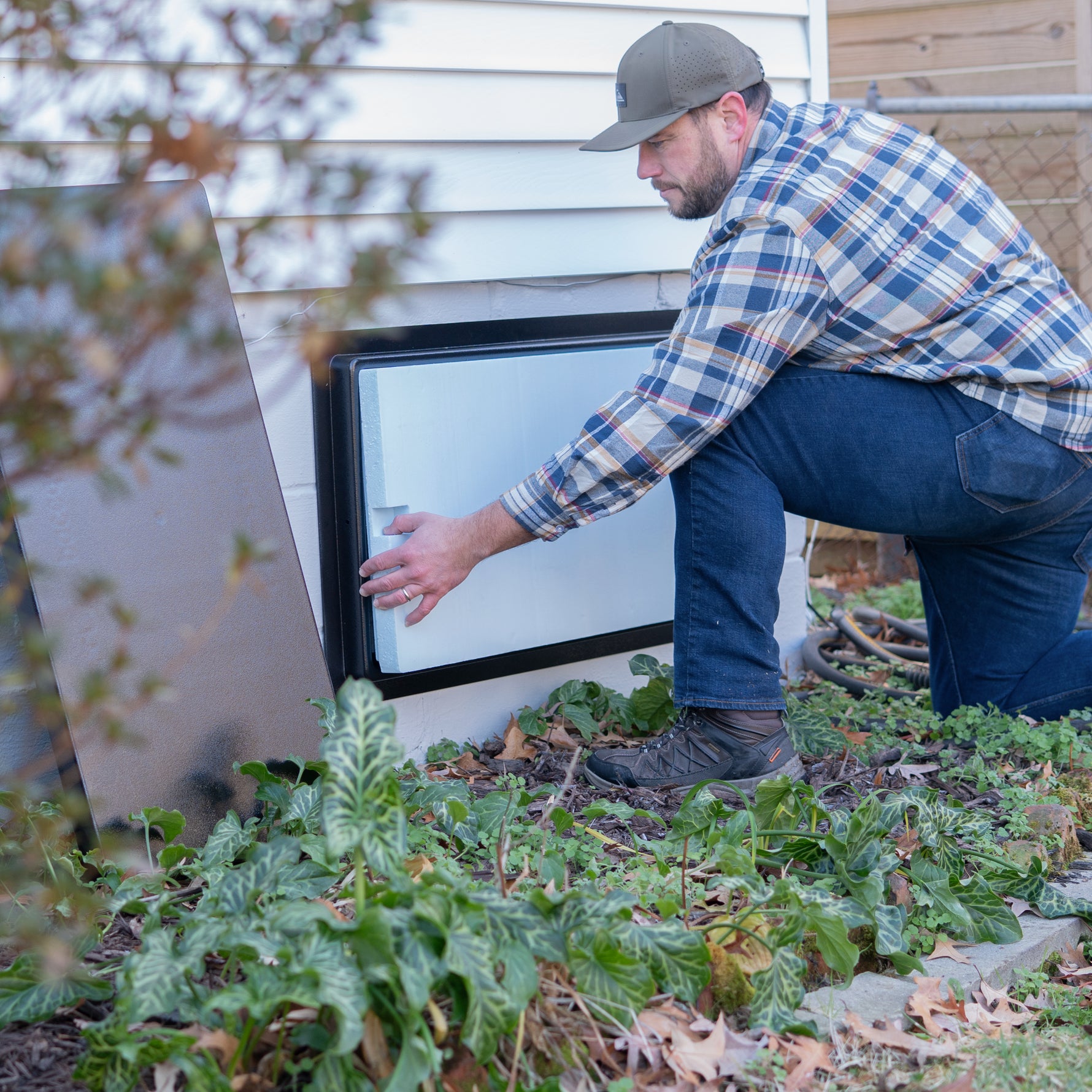 Man replacing insulation in crawl space door in a garden setting