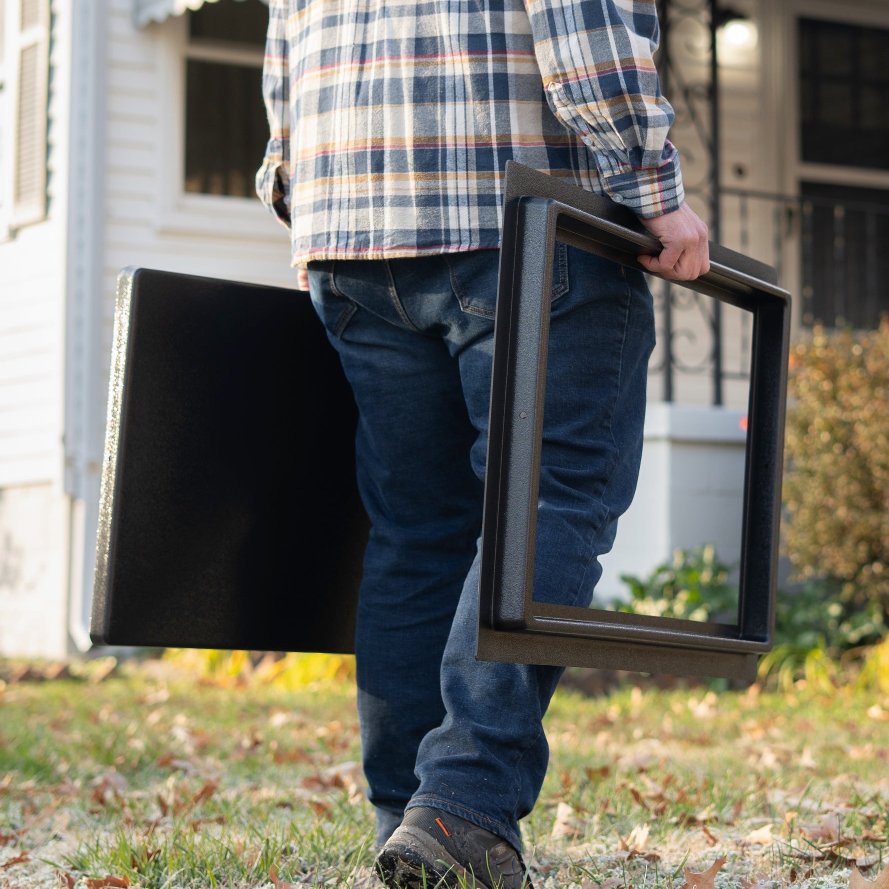 Person carrying two large black frames outdoors in front of a house.