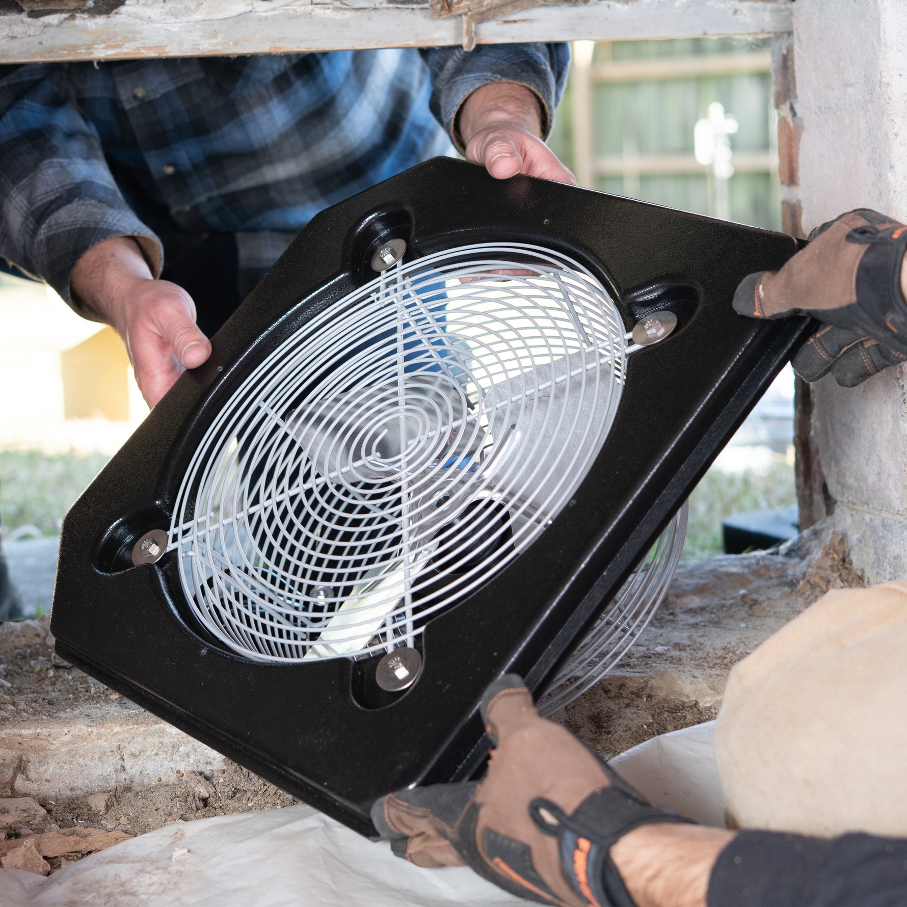 Person installing a large black outdoor fan with spiral design on a wooden structure.