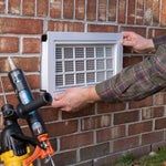 Person installing an air vent on a brick wall with tools nearby.