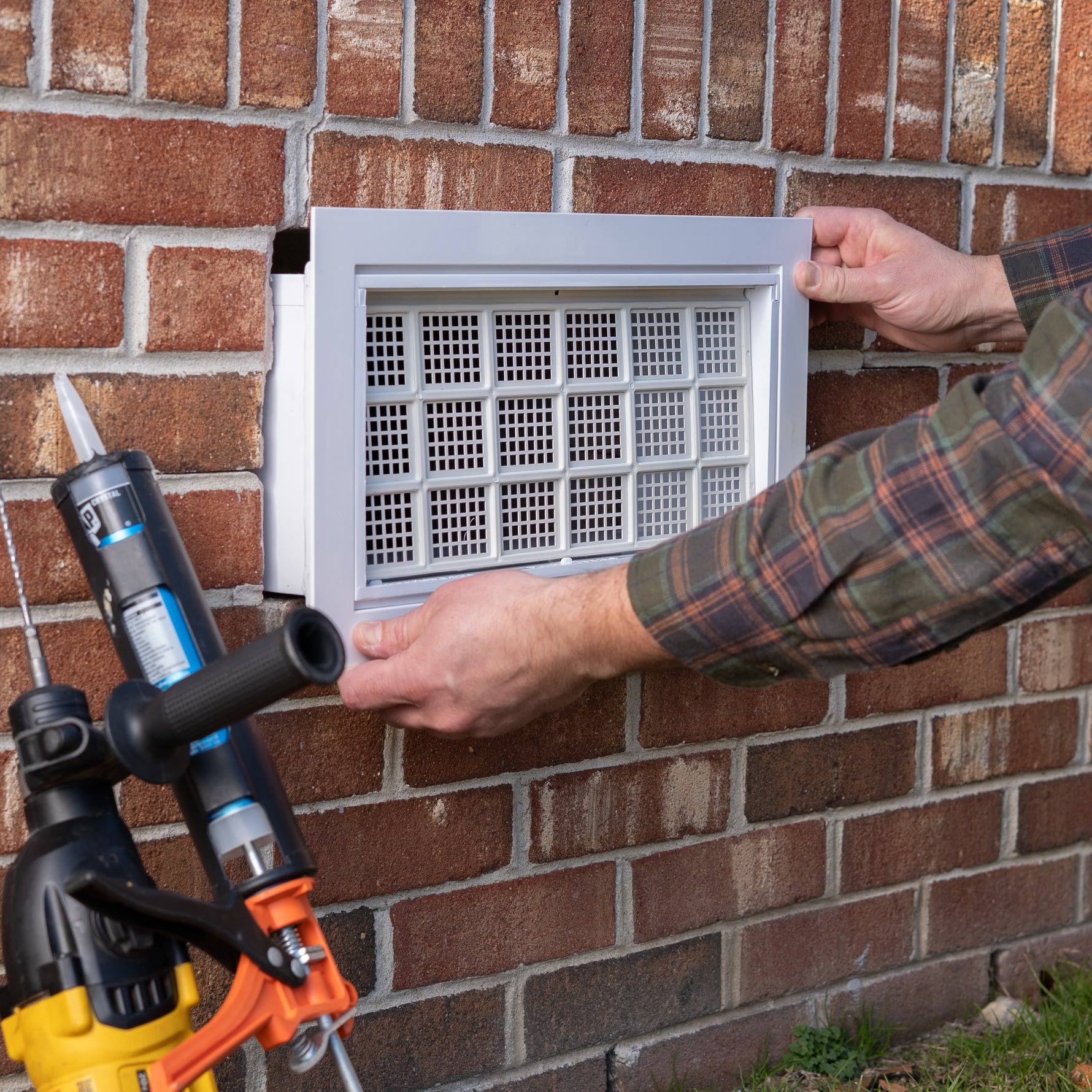 Person installing an air vent on a brick wall with tools nearby.