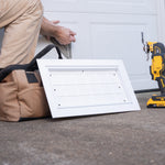 Person installing a white vent cover on a garage door with a tool in the background.