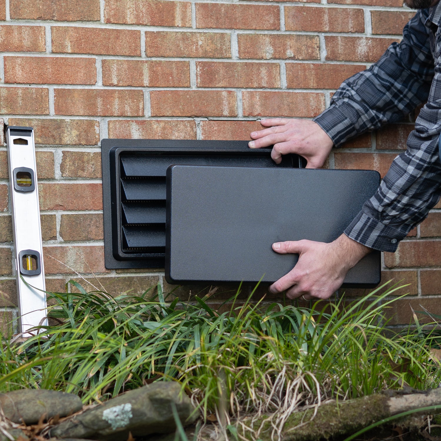 Person holding a black vent and cover against a brick wall