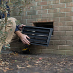 Person installing a black exterior wall vent on a brick wall.