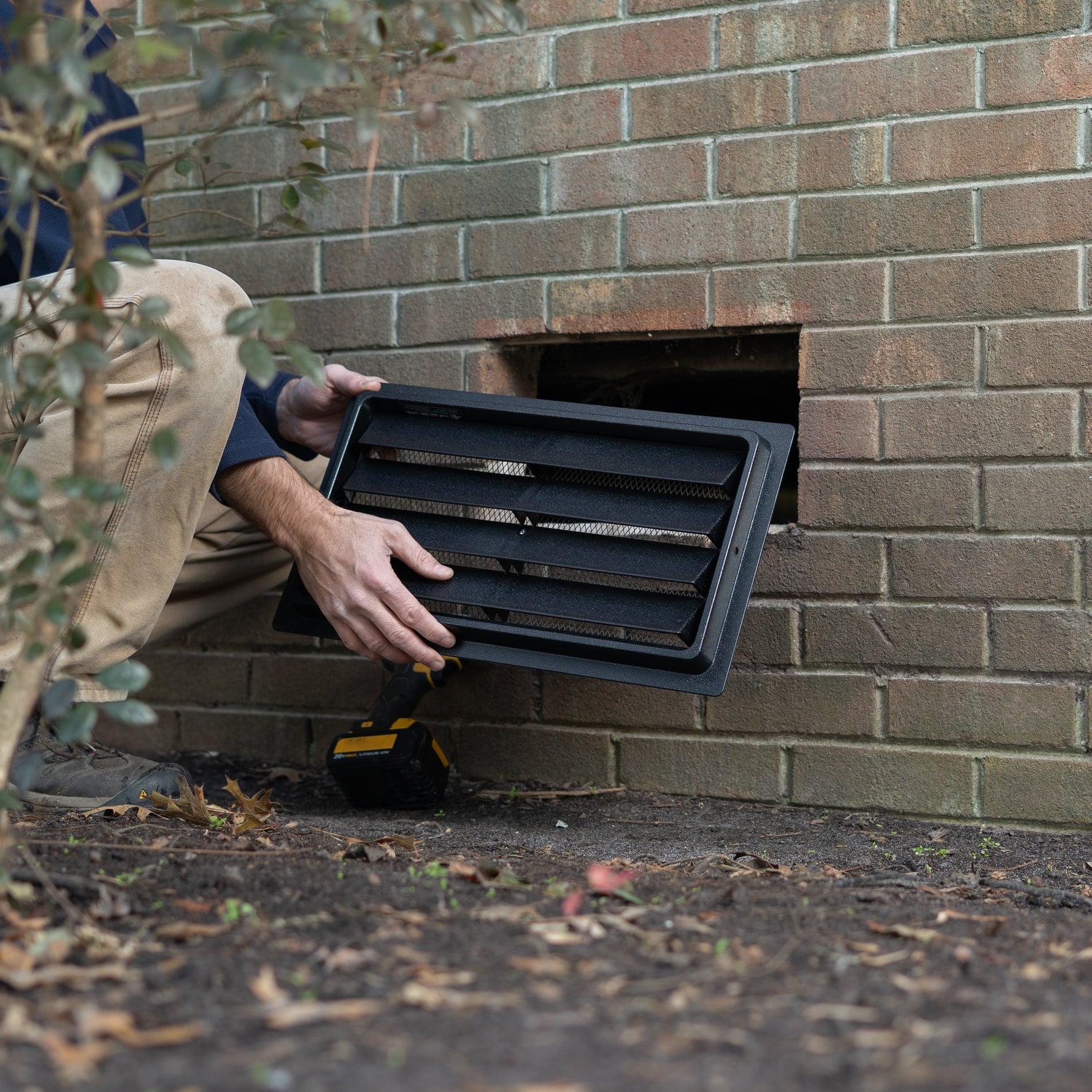 Person installing a black exterior wall vent on a brick wall.