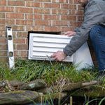 Person installing a white exterior foundation air vent on a brick wall.