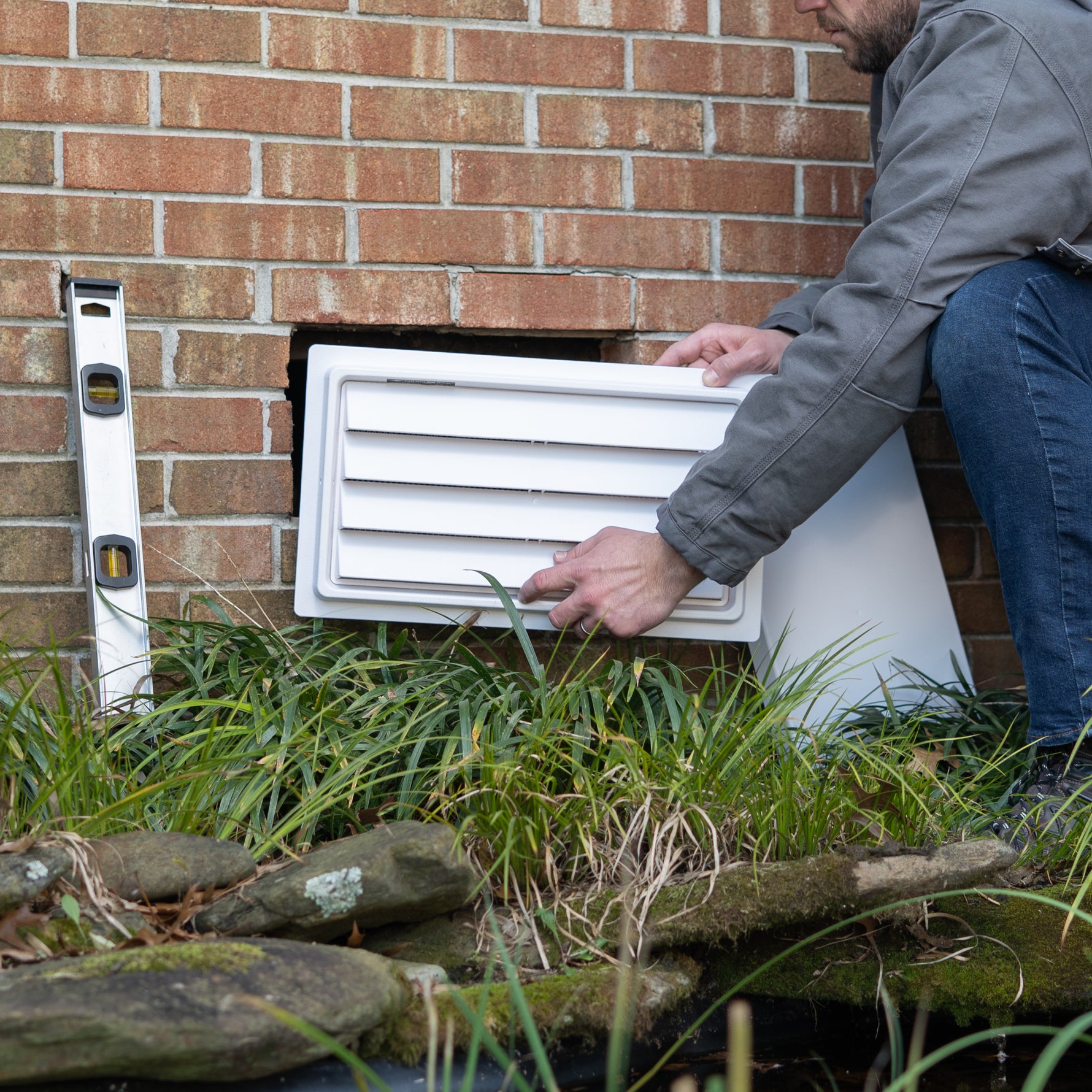 Person installing a white exterior foundation air vent on a brick wall.