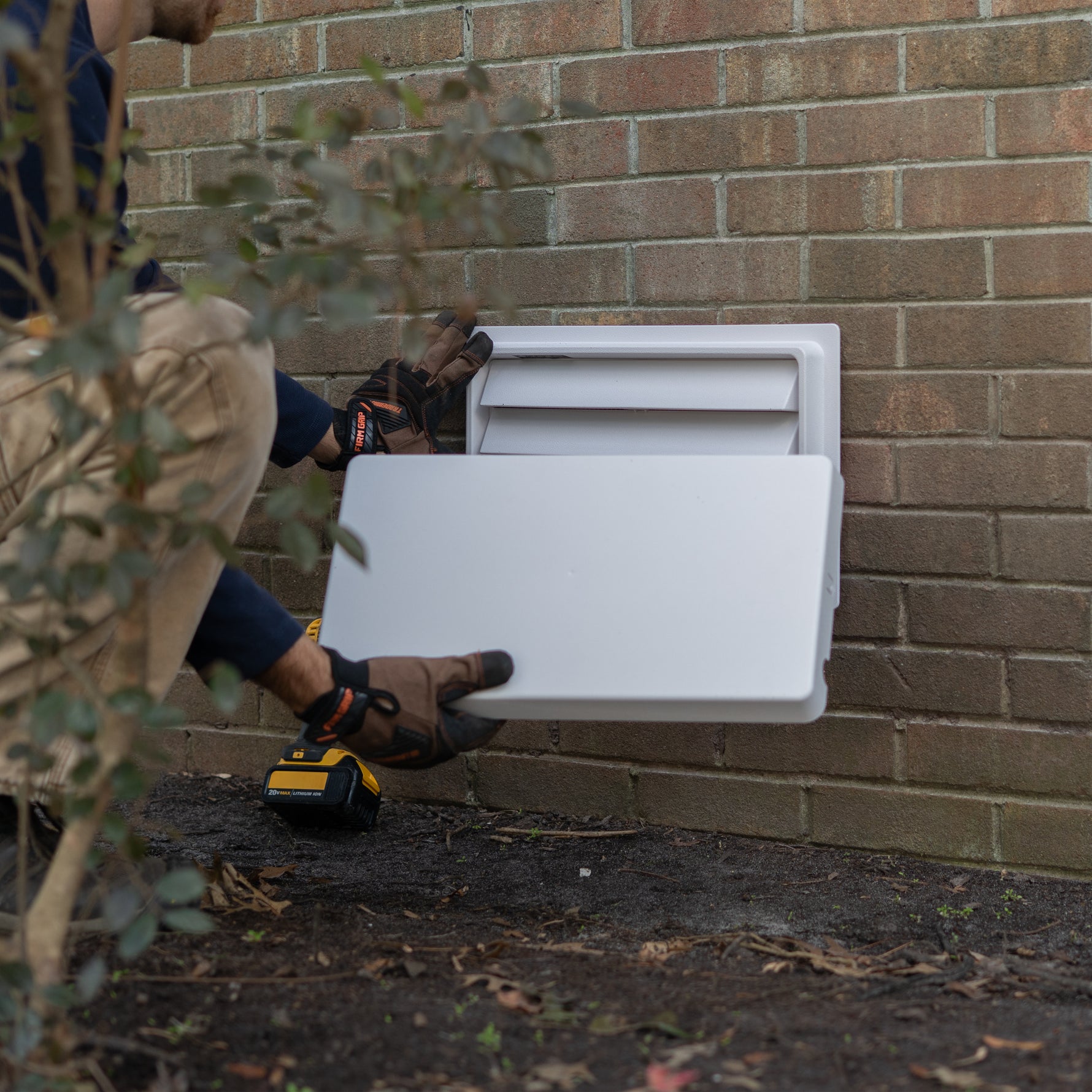 Person installing a white louvered air vent holding the cover on a brick wall