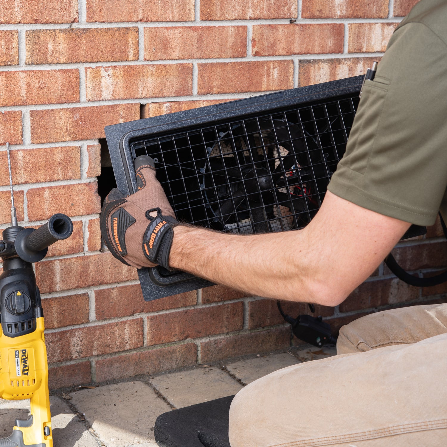 Person installing an air vent on a brick wall with a drill nearby.