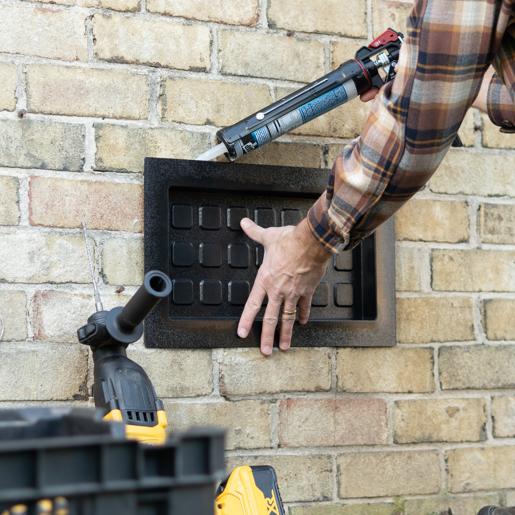 Person using a silicone adhesive to install a black vent cover with a toolbox in the foreground.