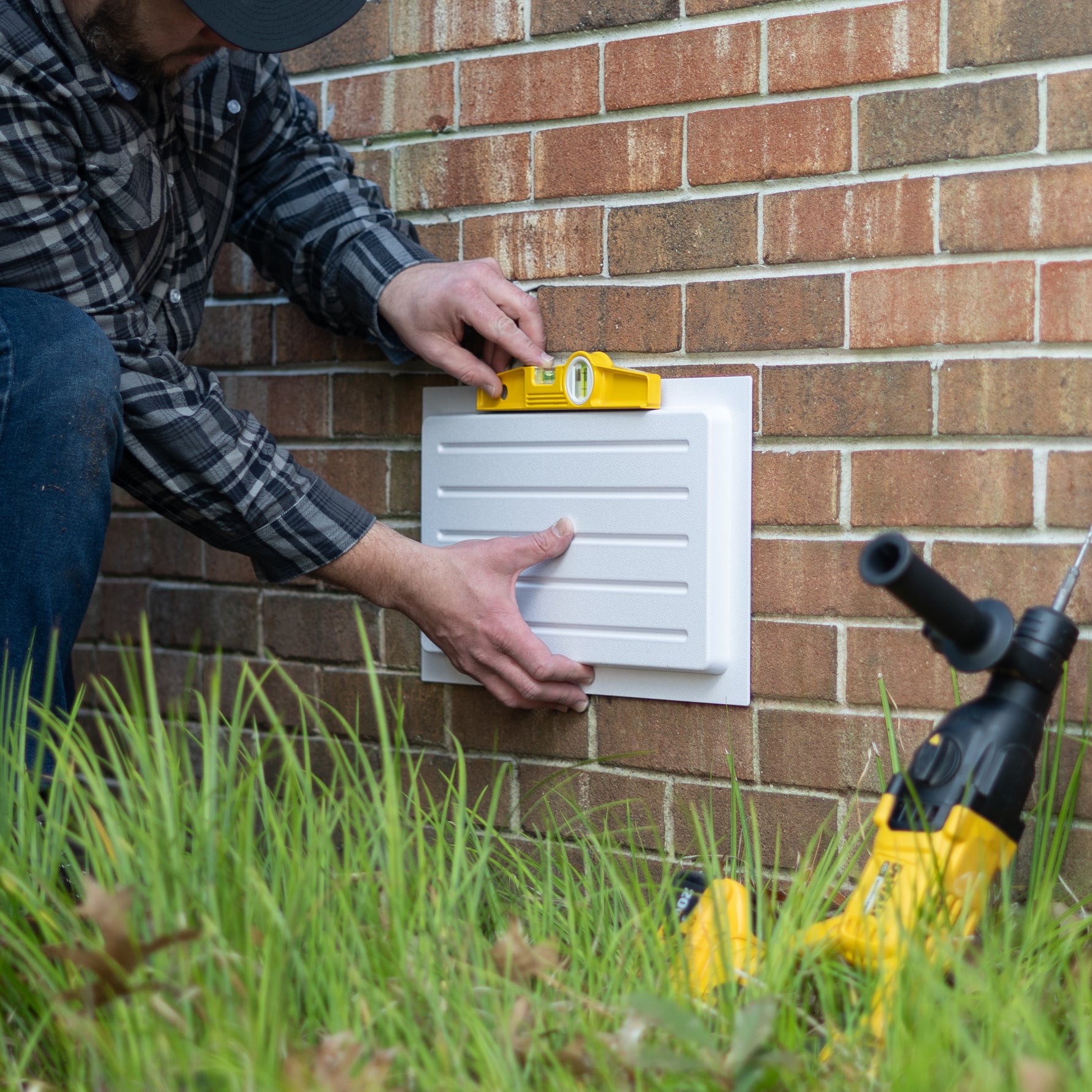 Person installing an exterior wall vent cover on a brick wall with tools nearby.