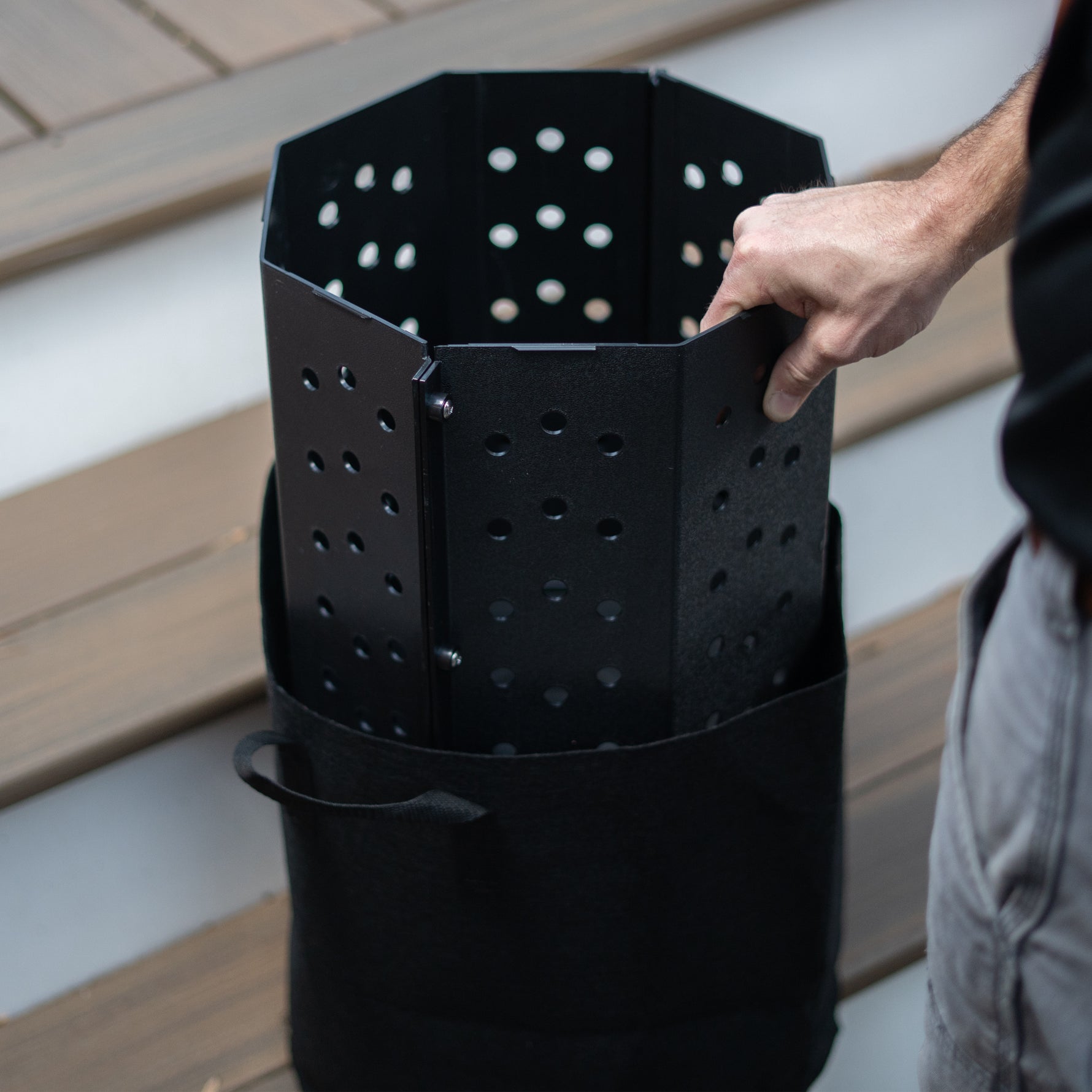 Person putting a black bin into a black geotext cloth bag against a wooden background