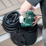 Person handling a green pump into a bucket with black hose and white filter on a wooden deck